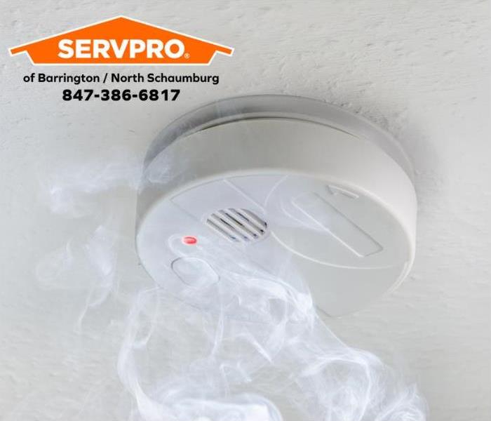 White smoke alarm with smoke on a white ceiling.